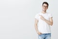 Portrait of charismatic relaxed and friendly young caucasian man in glasses and t-shirt pointing left at copy space