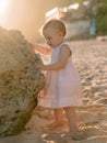 Portrait of charming baby girl in dress on sandy beach with sunset tones