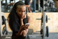 Portrait of charming black young woman with luxury long hair texting on her smartphone in the gym Royalty Free Stock Photo