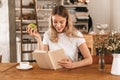 Portrait of charming blond woman reading book and eating green apple while sitting in cozy cafe indoor Royalty Free Stock Photo