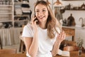 Portrait of charming blond woman talking on cell phone while standing in stylish wooden kitchen at home Royalty Free Stock Photo