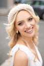 Portrait of charming blonde girl with grey eyes, pearl tiara on head and jewelry, brightly smile outdoor. Joyful bride. Royalty Free Stock Photo