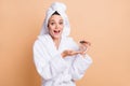 Portrait of charming cheerful amazed girl wear bathrobe holding in hand bottle aroma isolated over beige pastel color