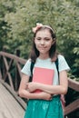 Portrait of a charming child holding a notebook, smiling in a white t-shirt with a backpack on his back, standing in the open air Royalty Free Stock Photo