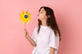 Charming playful little girl blowing at paper windmill, playing with pinwheel toy on stick. Royalty Free Stock Photo