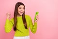 Portrait of charming delighted schoolgirl hold telephone raise fist celebrate empty space isolated on pink color