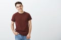 Portrait of charming friendly-looking boyfriend in red t-shirt, holding hand in pocket, tilting head and smiling