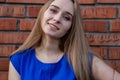 A cute girl in a blue blouse, with a chain around her neck, with long blond hair and blue eyes, smiles at the camera, against the Royalty Free Stock Photo