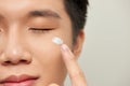 Portrait of a charming handsome young guy has healthy perfect skin, cream on his face, holds moisturizing cream on his face