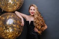 Portrait charming joyful young woman in black luxury dress, with long curly blonde hair, big balloons full with golden Royalty Free Stock Photo