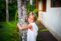 Portrait. Charming little girl standing and holding the tree, wearing white dress. Cute face. Spending time outdoor in Royalty Free Stock Photo