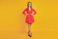 Portrait of charming positive woman hands hips wear red mini dress high-heels on yellow wall Royalty Free Stock Photo