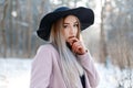 Portrait of a charming pretty young woman in a black elegant hat in a stylish warm pink coat on the background of a winter forest Royalty Free Stock Photo