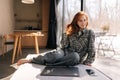 Portrait of charming redhead young woman sitting by window on sunny day relaxing at home looking at camera. Smiling calm Royalty Free Stock Photo