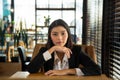 Portrait charming young Asian woman in formal wear sitting on brown sofa chair put her hands on wooden table and put her chin on Royalty Free Stock Photo