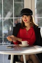 Portrait of Charming young woman in red sweater and stylish black coat, looking at camera in cozy cafe. Royalty Free Stock Photo