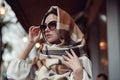 Portrait of charming young stylish woman in black sunglasses and plaid scarf on head at street. Royalty Free Stock Photo