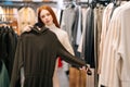 Portrait of charming young woman choosing clothes and looking to mirror in clothing store. Royalty Free Stock Photo