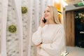Portrait of charming young woman talking using smartphone standing in hotel lounge. Cheerful blonde female talking Royalty Free Stock Photo