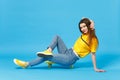 Portrait of charming young woman in vivid casual clothes looking camera and sitting with yellow skateboard isolated on