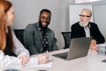 Portrait of cheerful African-American businessman sitting at table, sharing project ideas with mixed race investors at Royalty Free Stock Photo