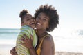 Portrait of cheerful african american mother and daughter with cheek to cheek at beach on sunny day Royalty Free Stock Photo