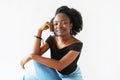 Portrait of a cheerful Afroamerican young woman sitting and looking at the camera on white background