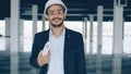 Portrait of cheerful Arab man architect holding blueprint and wearing helmet standing indoors empty building Royalty Free Stock Photo