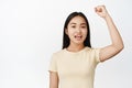 Portrait of cheerful asian girl raising her hand, protesting and chanting, looking encouraged, standing over white