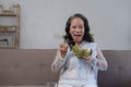 Portrait, Cheerful Asian 60s aged woman having breakfast in her living room, eating healthy salad vegetables mix bowl. Royalty Free Stock Photo