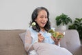 Portrait, Cheerful Asian 60s aged woman having breakfast in her living room, eating healthy salad vegetables mix bowl. Royalty Free Stock Photo