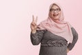 Portrait of cheerful Asian woman with hijab, making fun face with peace sign hand gesture. Advertising concept. Isolated image on Royalty Free Stock Photo