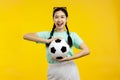 Portrait of Cheerful Asian woman holding a soccer ball isolated on yellow background, football concept Royalty Free Stock Photo