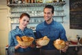 Portrait of cheerful baristas offering breads at coffee shop