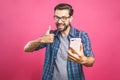 Portrait of a cheerful bearded man taking selfie and showing thumbs up gesture over pink background. Isolated