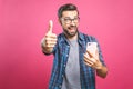 Portrait of a cheerful bearded man taking selfie and showing thumbs up gesture over pink background. Isolated