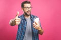 Portrait of a cheerful bearded man taking selfie and showing thumbs up gesture over pink background. Isolated