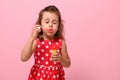 Portrait of cheerful beautiful baby girl blowing soap bubbles, isolated over pink background with copy space. Gorgeous child Royalty Free Stock Photo