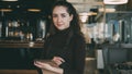 Portrait of cheerful and beautiful young waitress standing, keeping menu, and smiling sincerely in slylish cafe. Royalty Free Stock Photo