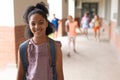 Portrait of cheerful biracial girl wearing backpack standing in school corridor, copy space Royalty Free Stock Photo