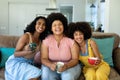 Portrait of cheerful biracial young female friends holding coffee cups relaxing on sofa at home Royalty Free Stock Photo