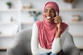 Cheerful Black Muslim Woman In Hijab Talking On Mobile Phone At Home