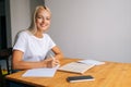 Portrait of cheerful blonde female student writing notes or essay, studying, reading textbook, sitting at table with Royalty Free Stock Photo