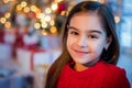 Portrait of a cheerful brown-eyed baby in red dress against background of a Christmas tree and boxes with gifts Royalty Free Stock Photo