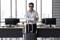 Portrait of cheerful business man holding passport and luggage in workplace of office. Summer vacations concept Royalty Free Stock Photo