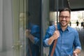 Portrait of cheerful businessman carrying laptop bag standing by window in the city