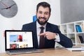 portrait of cheerful businessman pointing at laptop at workplace