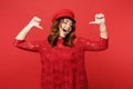 Portrait of cheerful confident young woman in lace dress cap pointing thumbs on herself isolated on bright red wall