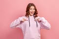 Portrait of cheerful curly haired teenage girl in hoodie pointing fingers at herself and surprisingly smiling at camera, wonder Royalty Free Stock Photo