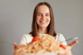 Portrait of cheerful delighted Caucasian woman with dark hair taking delicious noodles, having lunch isolated over gray background